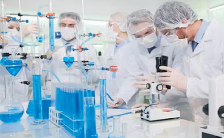 Mavi sıvılı test tüpleri ve cam malzemelerle çalışan laboratuvar ekibi