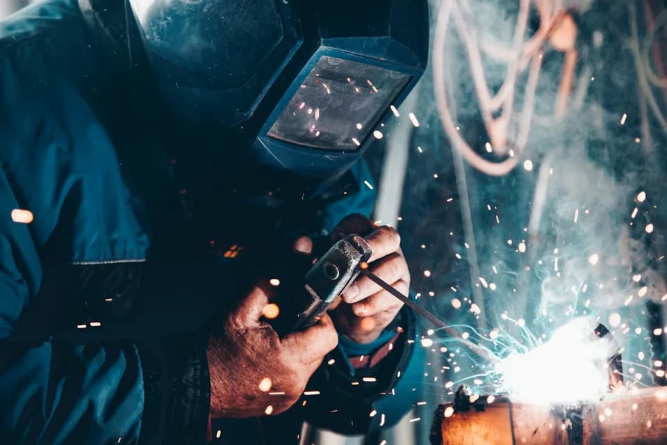 Maskeli kaynakçı kıvılcımlar saçarak metal kaynağı yapıyor